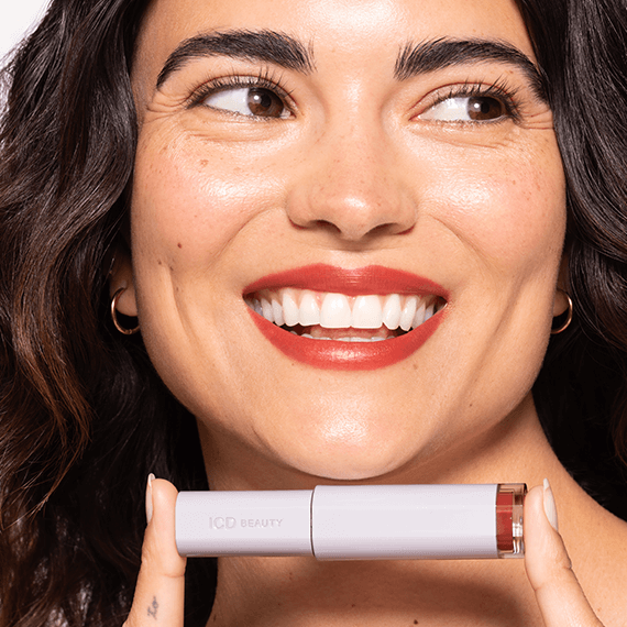 Woman smiling while holding ICD Makeup Butter Lip Tint Semi Matte, showcasing its rich color and radiant shine.