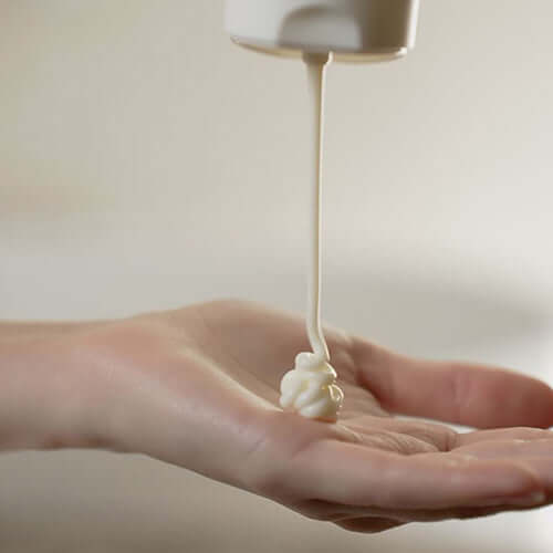 Suumel Nourishing Body Cream being poured onto a hand, showcasing its rich, creamy texture.