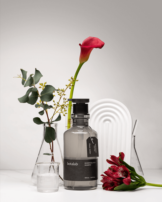 Riman Botalab Deserticola Plus Shampoo with flowers and greenery in a stylish setup, showcasing its nourishing qualities.
