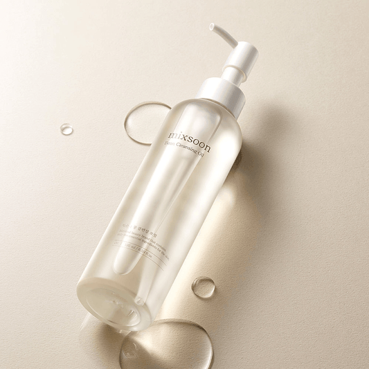 mixsoon Bean Cleansing Oil in a clear bottle on a beige background with droplets of cleansing oil.