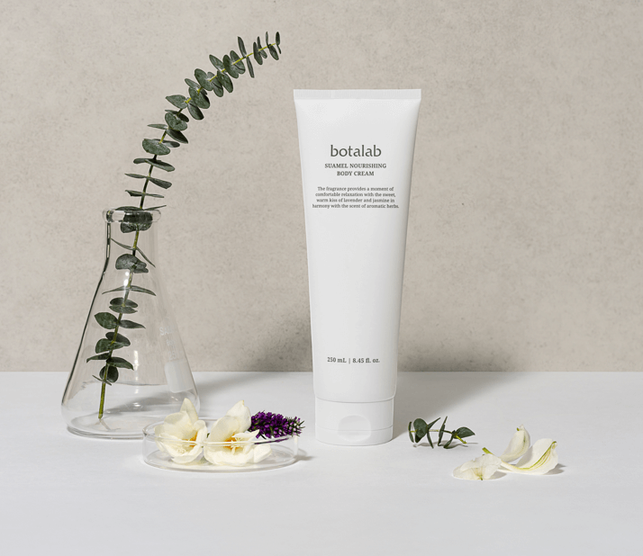 Suamela Nourishing Body Cream tube beside fresh flowers and eucalyptus on a neutral background.