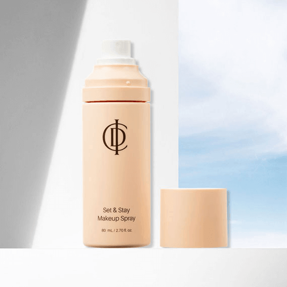 Riman ICD Makeup Set & Stay Makeup Spray bottle with cap against a bright sky backdrop.