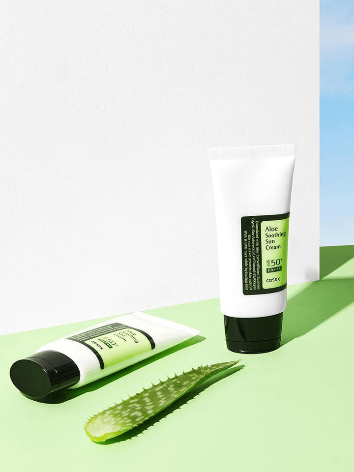 COSRX Aloe Soothing Sun Cream SPF50 | Korean Face Sunscreen tubes with aloe leaf on green background.