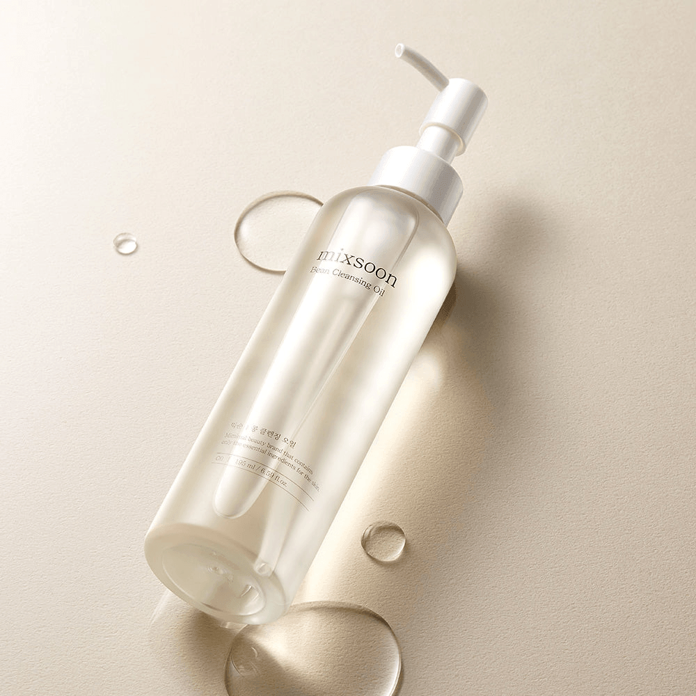 mixsoon Bean Cleansing Oil in a clear bottle on a beige background with droplets of cleansing oil.
